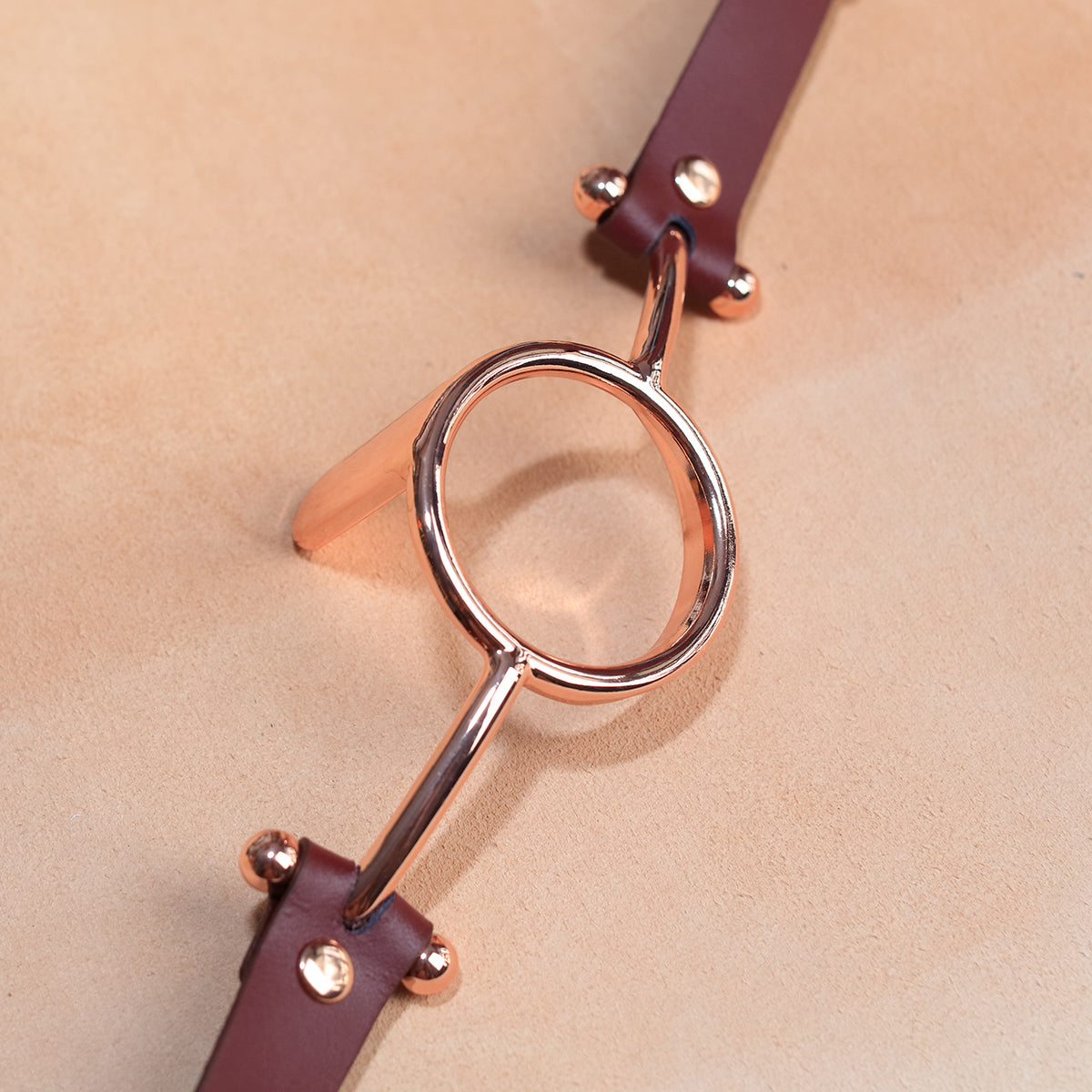 Close-up of luxurious gold metal O-ring tongue depressor gag with black premium vegan leather straps for oral bondage and deepthroat training by Sexy Maker.