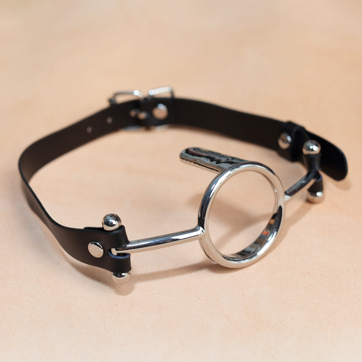 Close-up of metal O-ring tongue depressor gag with black premium vegan leather straps for oral bondage and deepthroat training by Sexy Maker.