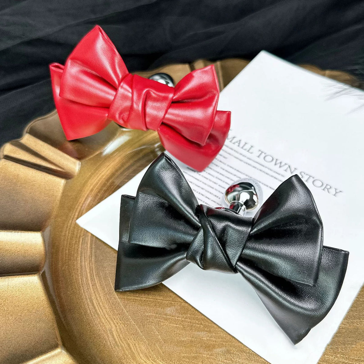 Front view of the Glossy Bow Anal Plug featuring a polished metal body and a black faux-leather ribbon, available on SexyMaker.