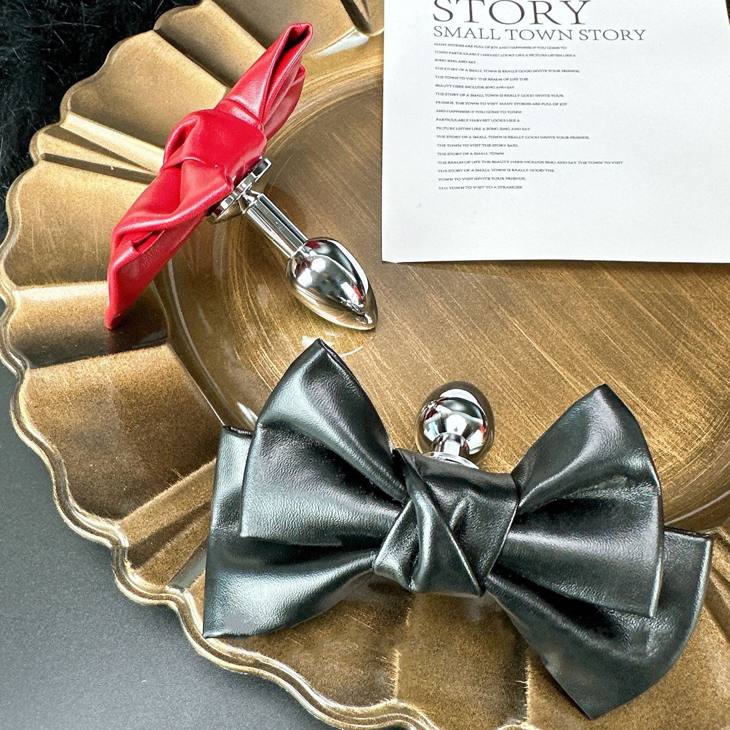 Front view of the Glossy Bow Anal Plug featuring a polished metal body and a black faux-leather ribbon, available on SexyMaker.